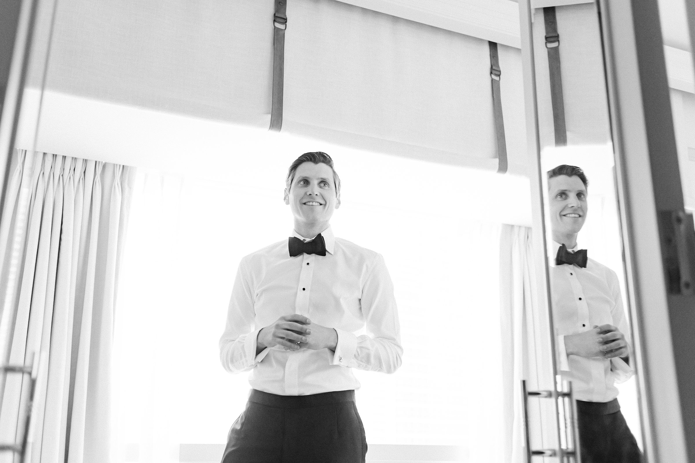 black and white image of the groom getting ready with his reflection and bow tie