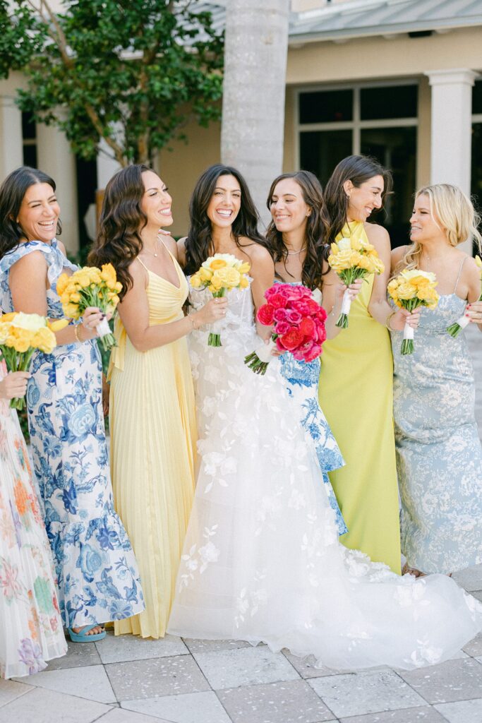 candid photo of the bride and bridesmaids laughing. Bridesmaids wearing yellow and blue dresses while holding yellow rose bouquets