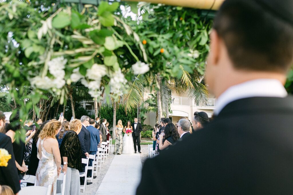 groom seeing the bride walk down the sandy aisle with palm trees in the background