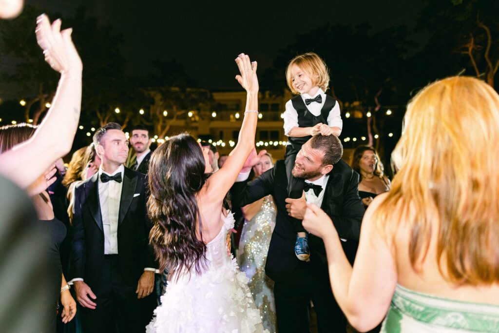 ring bearer on his fathers shoulders dancing with the wedding guests