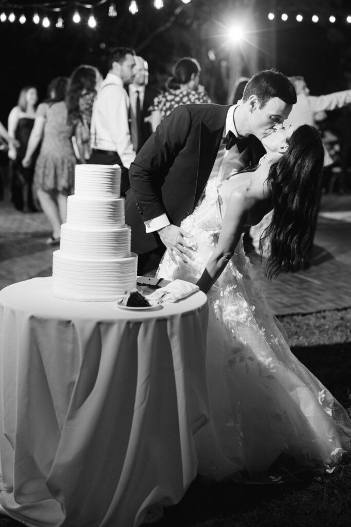 black and white image of the newlyweds cutting the cake and him dipping her.