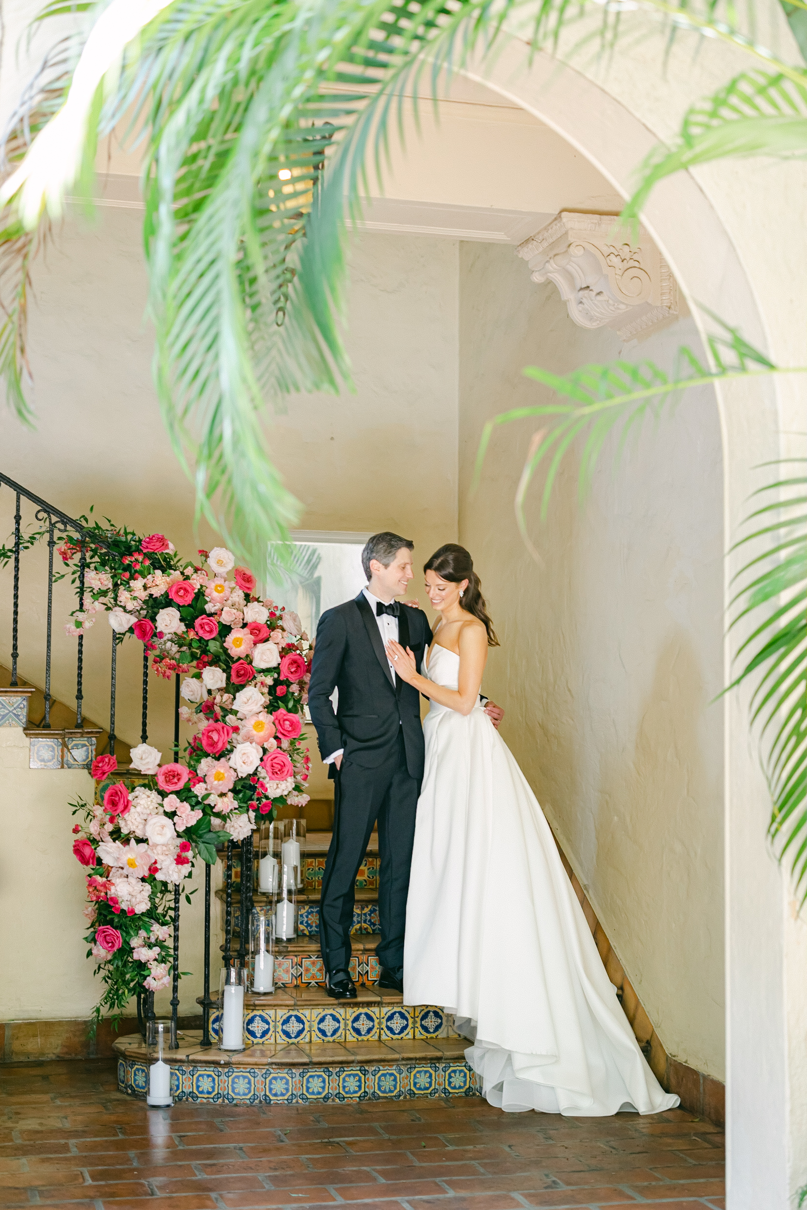 Bride and groom posing for an editorial portrait on a staircase. Staircase rail decorated in Barbie pink florals.