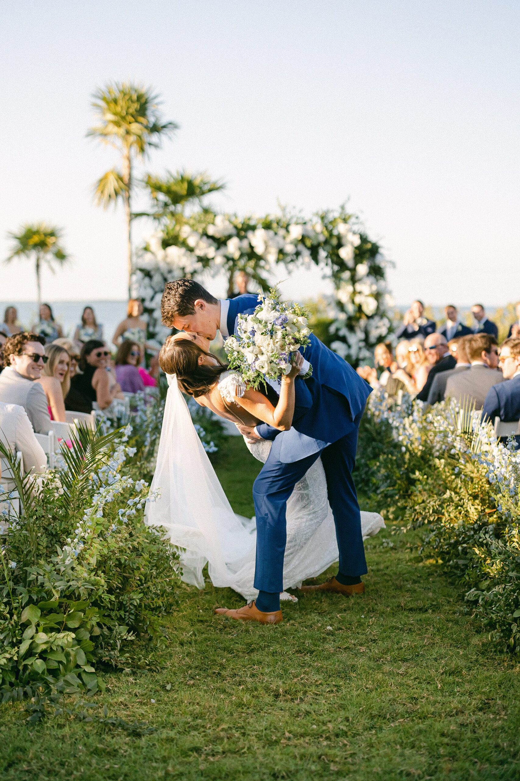 groom dips the bride in the middle of the luscious green aisle and kisses her in front of their guests