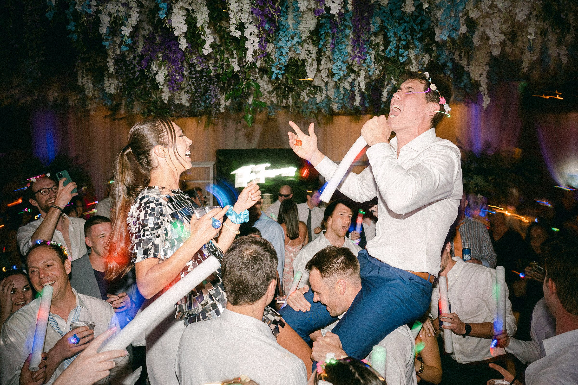 bride and groom singing during the reception while on guests shoulders
