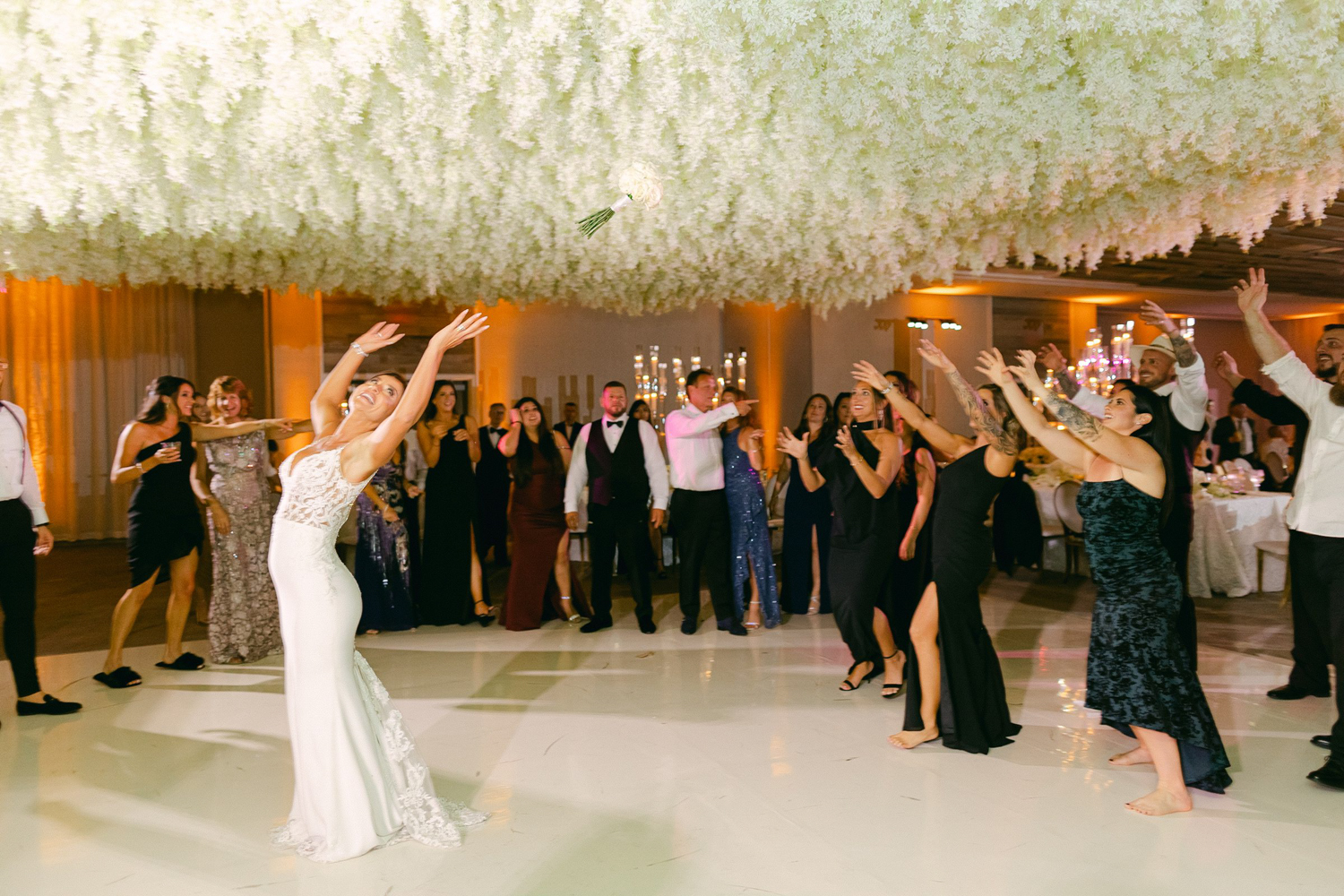 Bride tossing the bouquet to bridesmaids under the white orchid ceiling installation