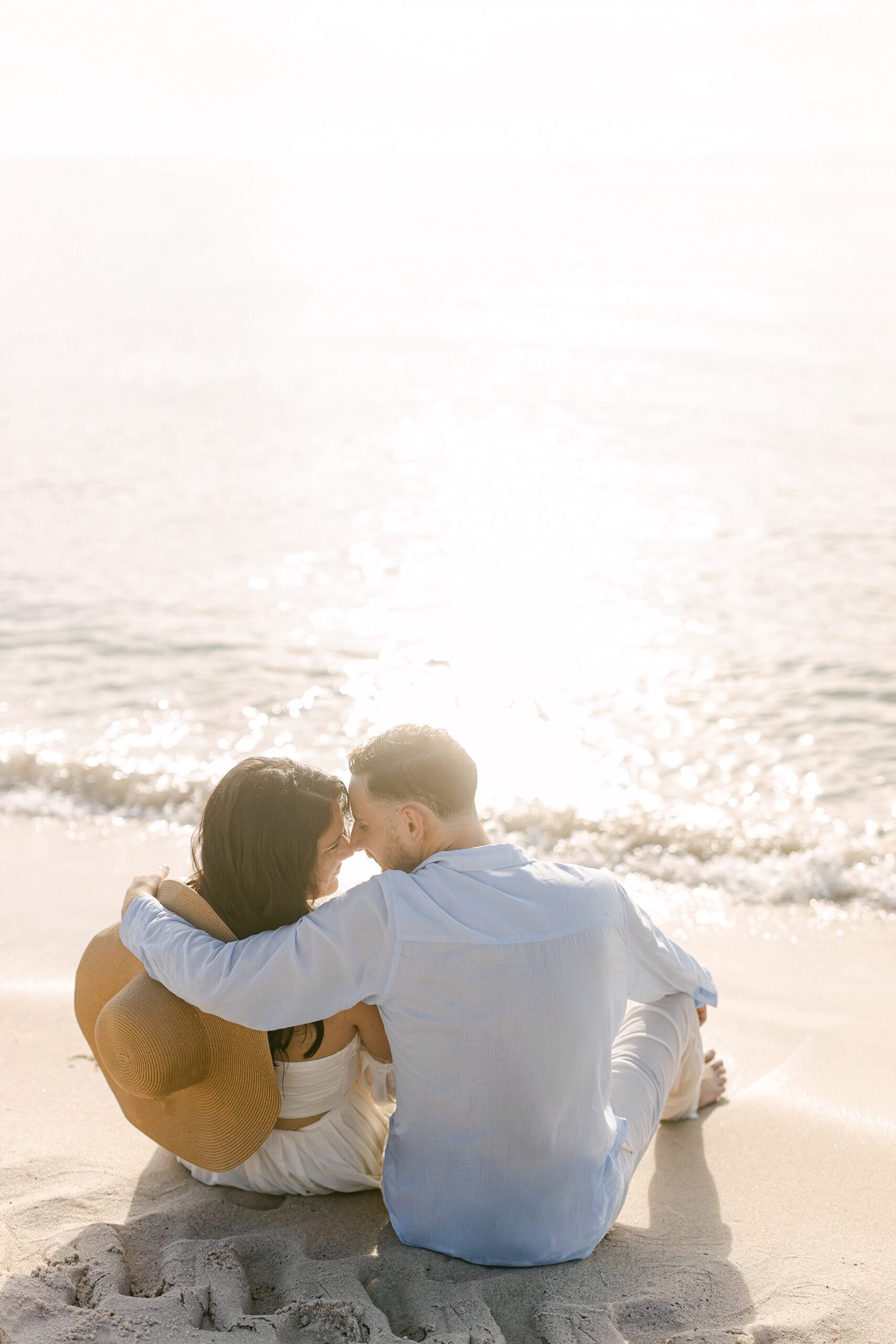 Couple sitting down on the sand looking at each other with the sunrise behind them