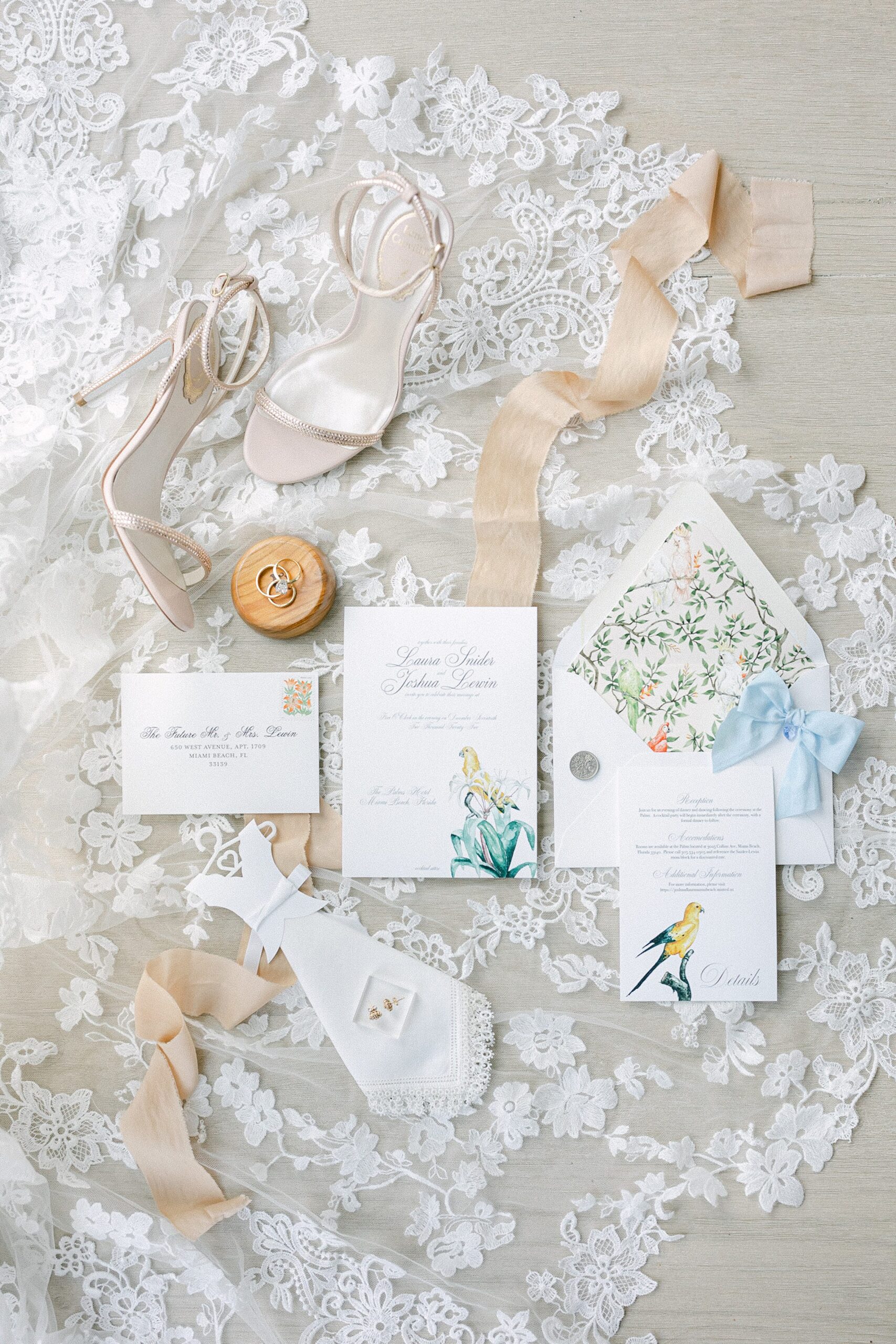 a lay flat composition of wedding stationary, rings, shoes on top of her lace veil