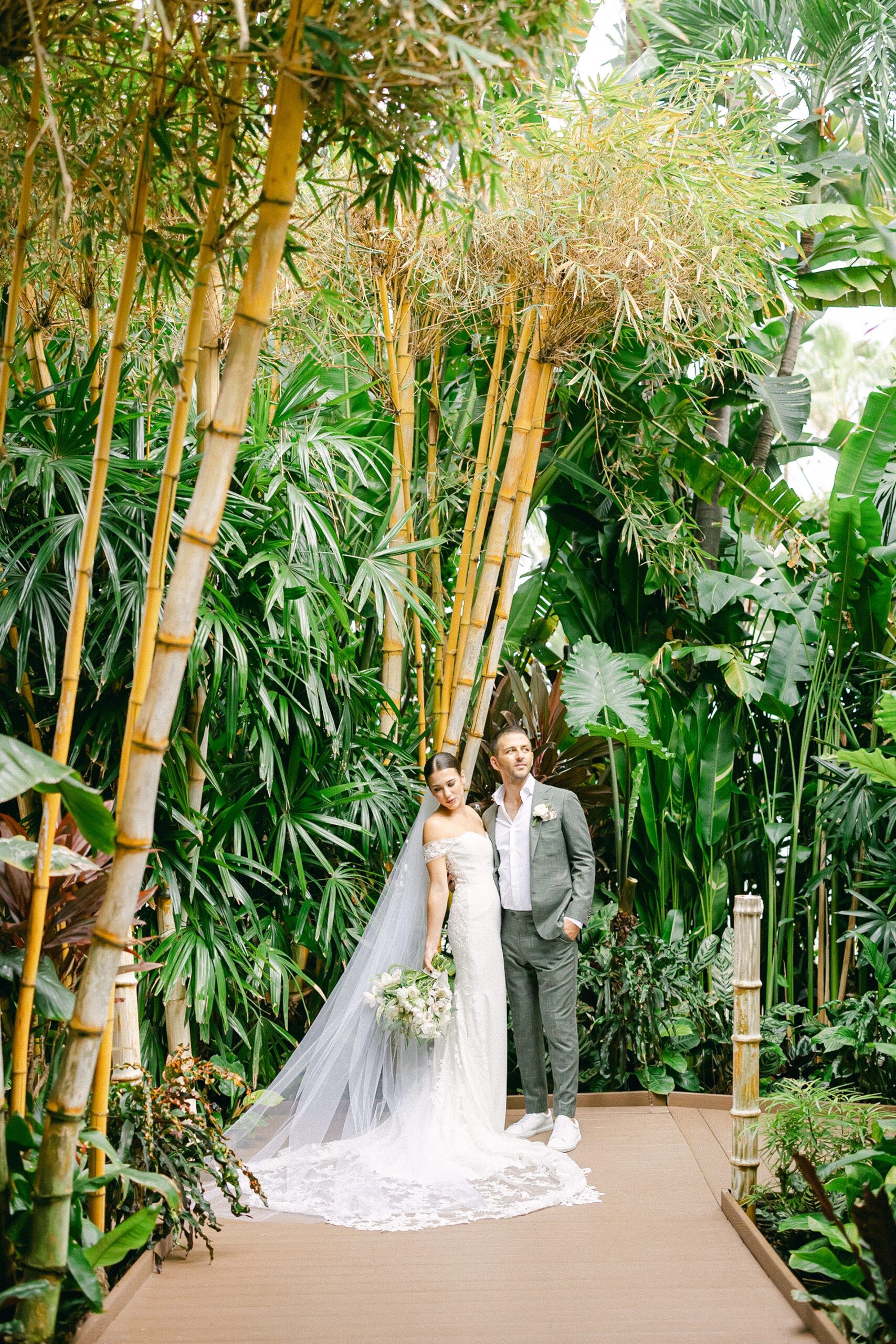 bride and groom posing looking away from each other in in the bamboo tree nook at the tropical garden
