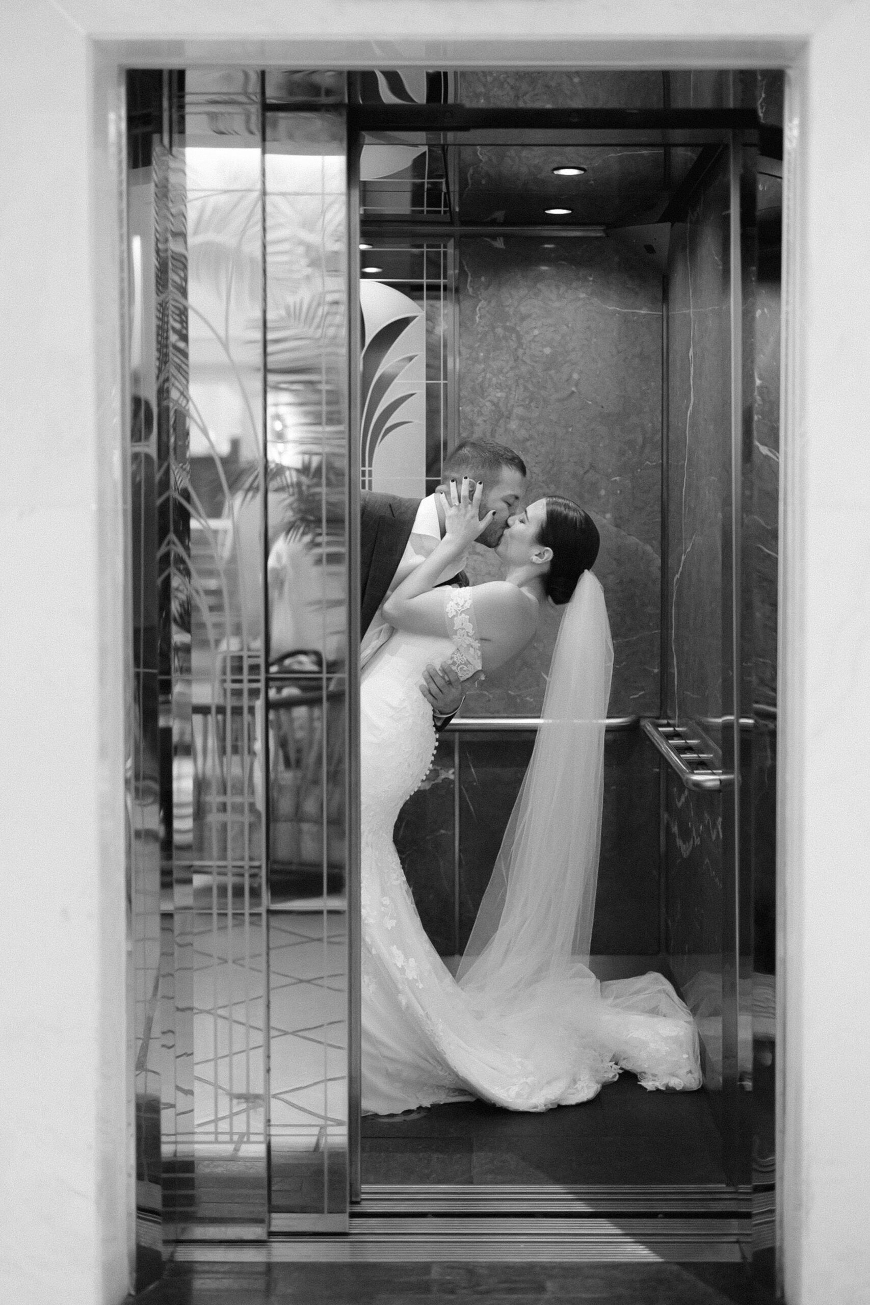 romantic black and white image of the bride and groom kissing in the elevator before it closes
