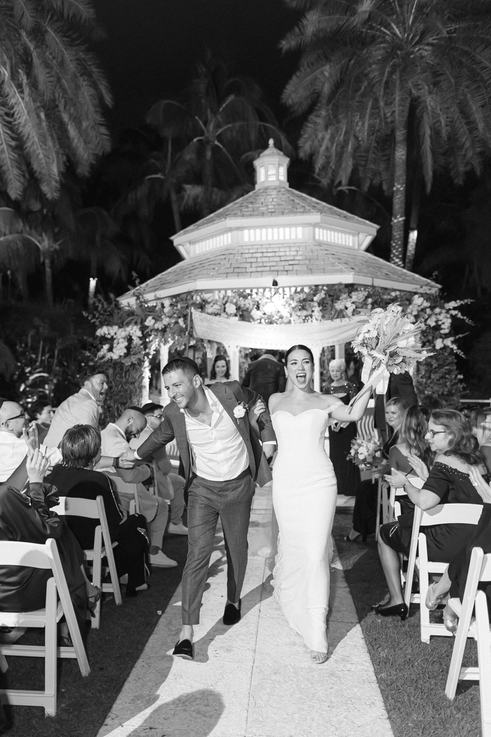 black and white image of the bride and groom running down the aisle with joy